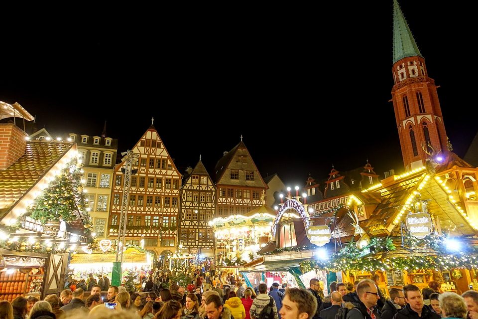 A German Christmas market at night: lit wooden stalls beneath half-timbered gabled houses.