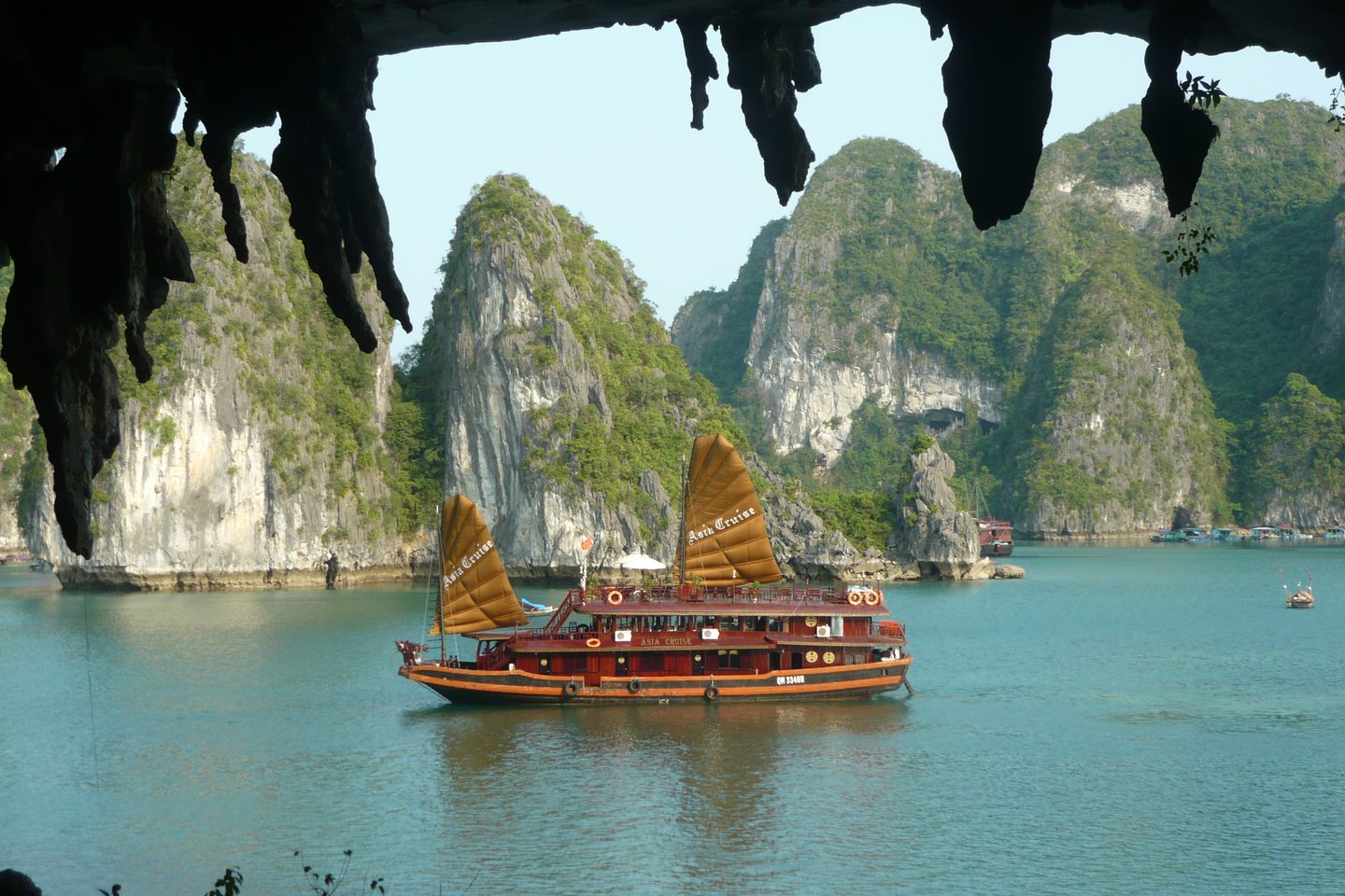 A traditional junk boat with ochre sails on Ha Long Bay, framed by limestone karsts and the mouth of a sea cave.