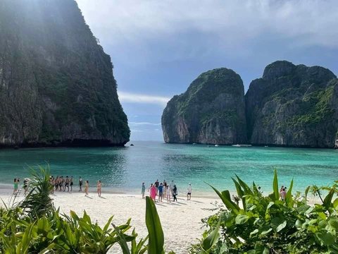 Limestone cliffs rising out of turquoise water at the Phi Phi Islands, longtail boats moored on the beach.